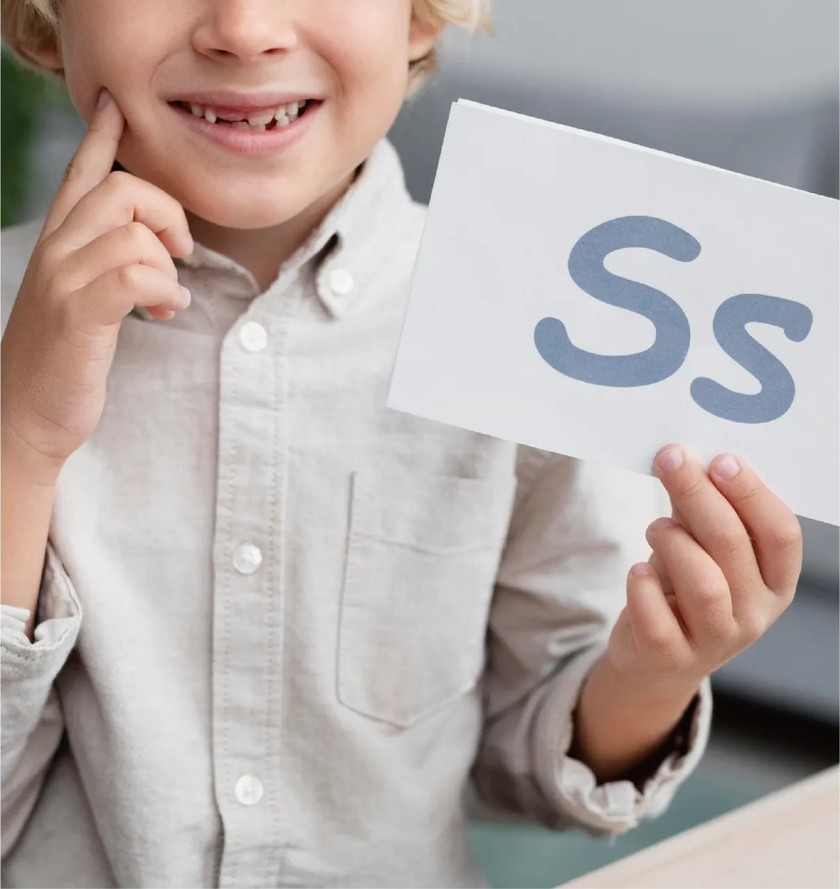 A smiling child holding a paper with Ss written on it
